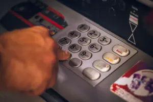 Ruka stiskající tlačítko na klávesnici bankomatu v Brazílii, zdůrazňující digitální bankovnictví.
