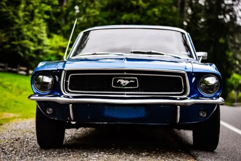 Detailní záběr na klasický modrý Ford Mustang zaparkovaný podél malebné silnice.