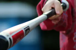 Detailní záběr na ruku svírající baseballovou pálku, ukazující akci a sportovní vybavení.