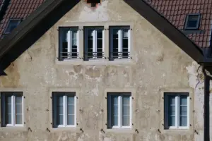 Detailní záběr na starou fasádu evropského domu s několika okny a rustikální texturou.