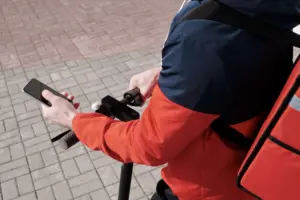 Doručovatel jezdící na elektrické koloběžce, který používá chytrý telefon k navigaci venku.