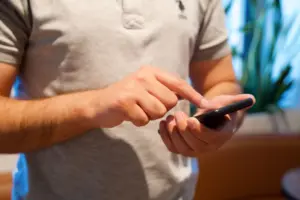Dospělý muž používající smartphone v jasném vnitřním prostředí, soustředěný na zařízení a interakci.